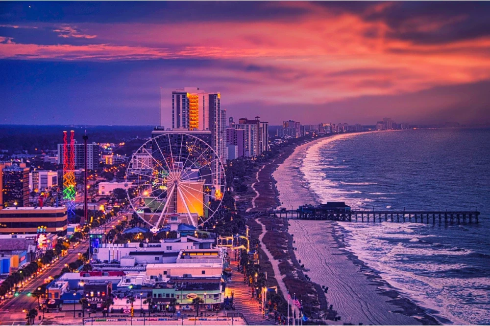 Vibrant Sunset Over A Coastal City Boardwalk And Ferris Wheel Next To The Ocean.